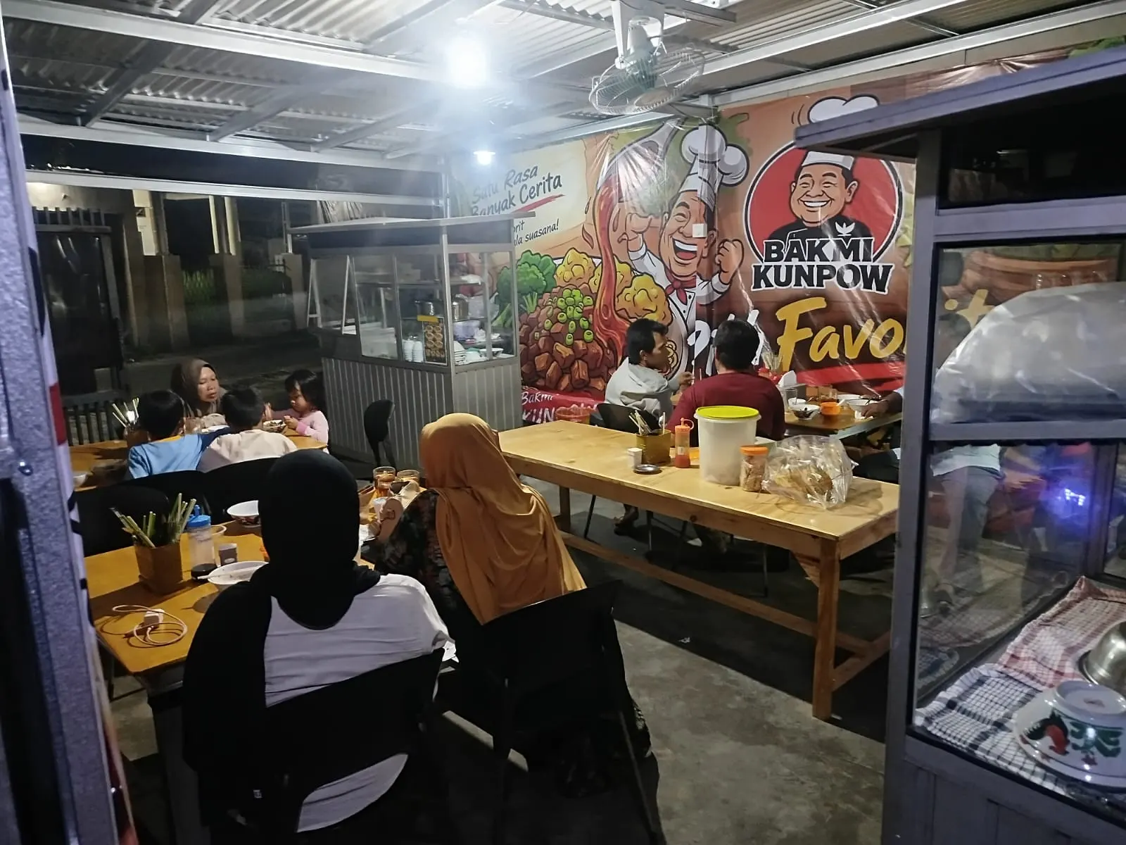 Suasana makan malam di warung Bakmi Kunpow, keluarga duduk di meja kayu